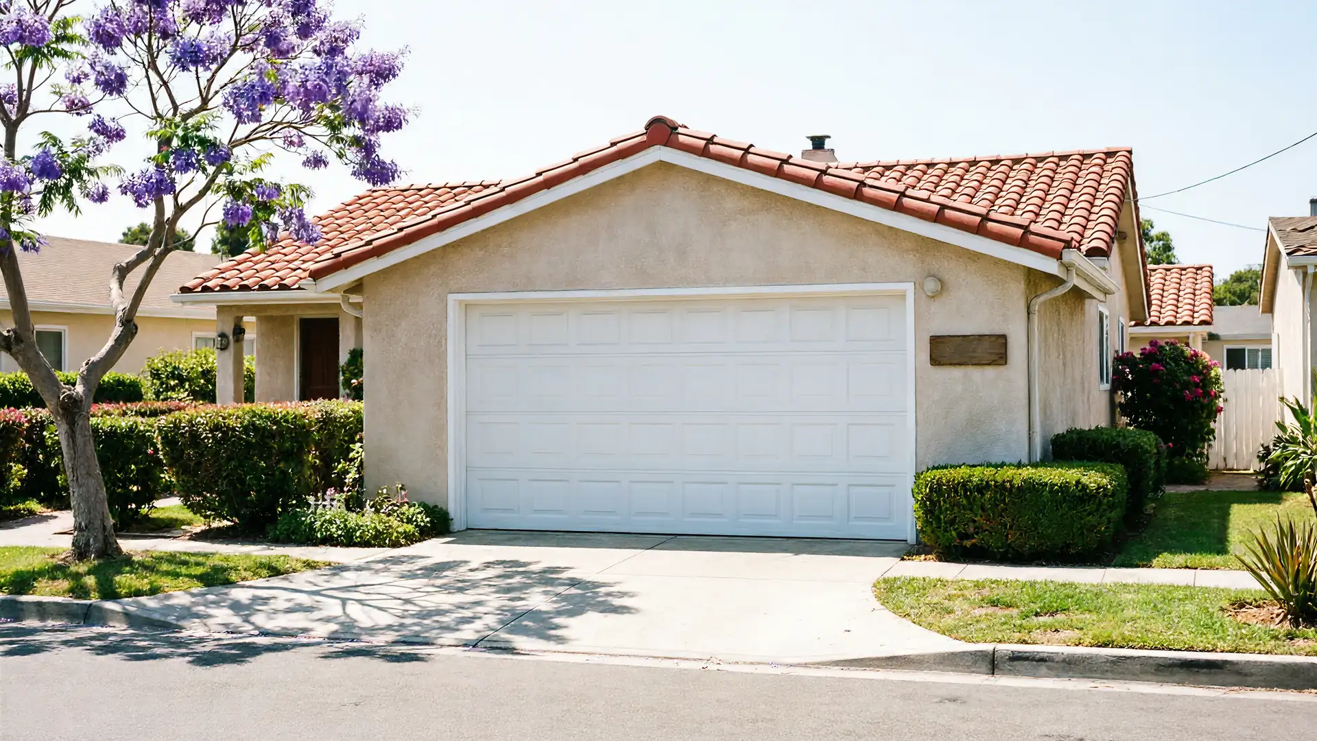 The house has a white garage door, a tiled roof, and a purple flowering tree.