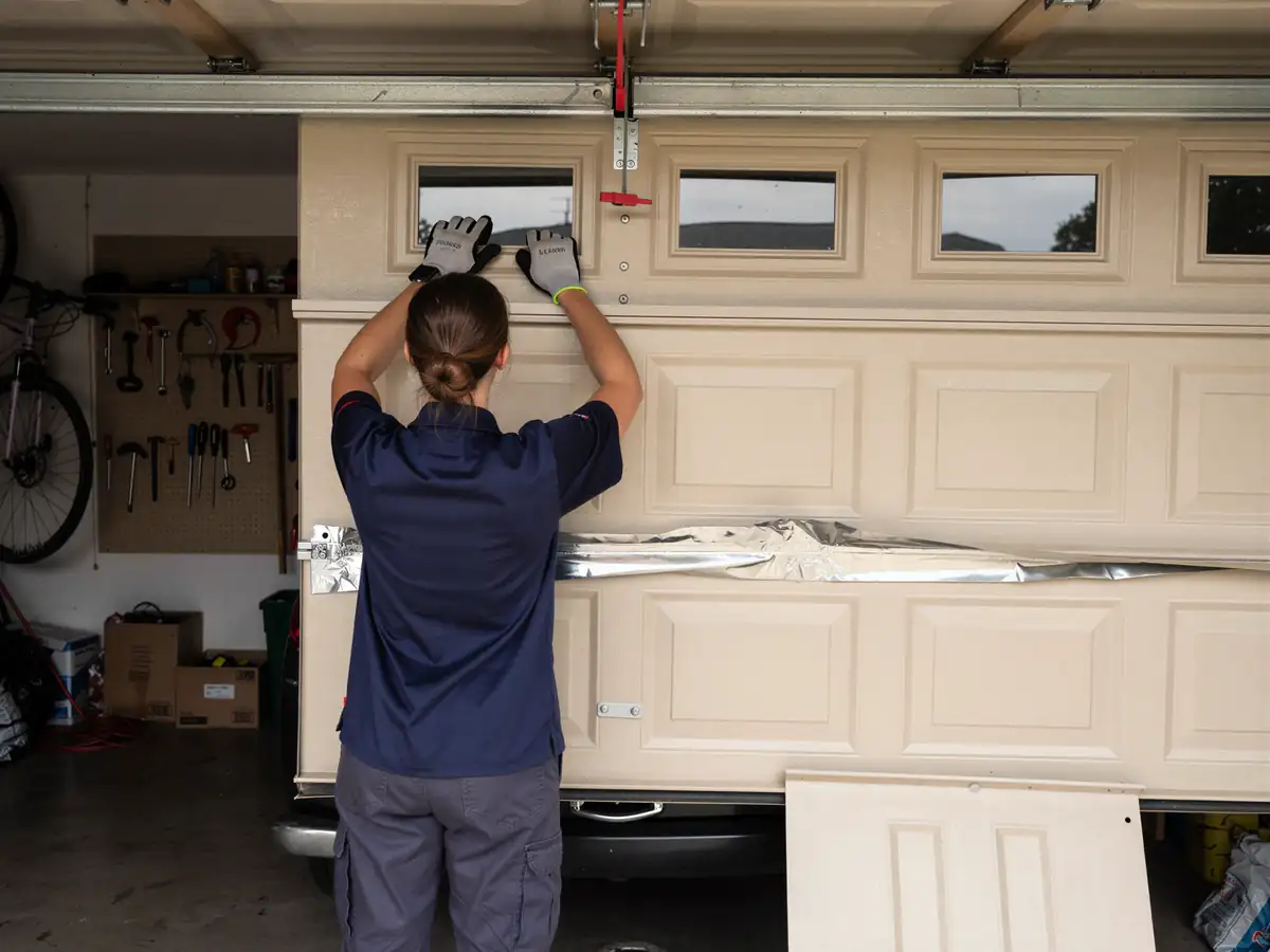A technician installs a new tan garage door with windows.